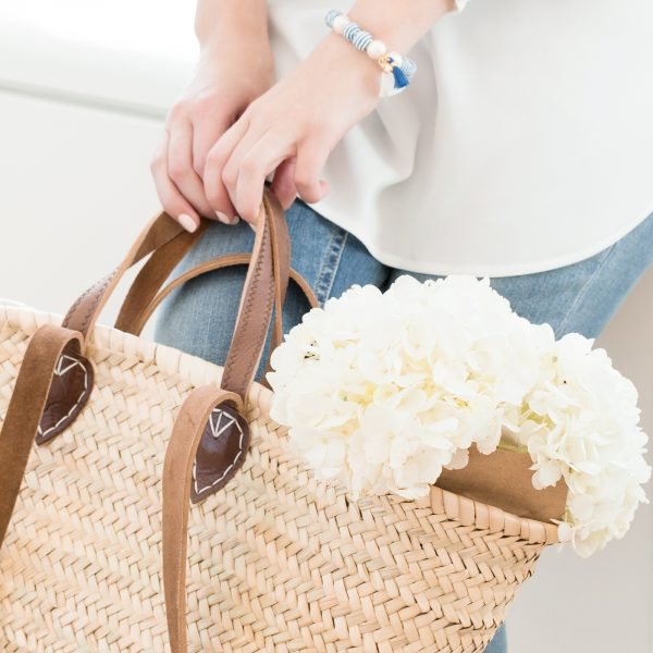A woman in blue jeans and white shirt holding a basket bag with some white hydrangea flowers in them.