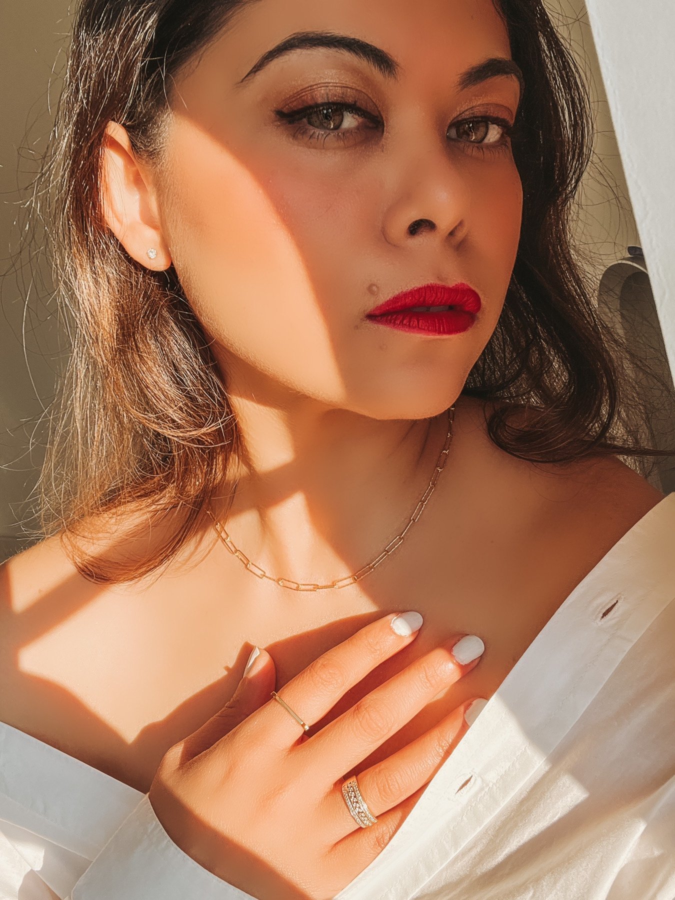 Monica Vinader gold jewellery on girl with red lips, white shirt and white nails.