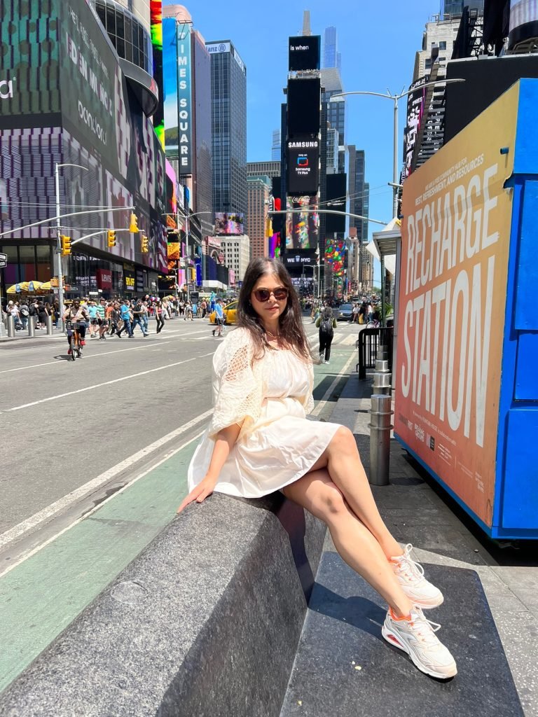 A picture of a beautiful woman sitting on a bench in front of Times square