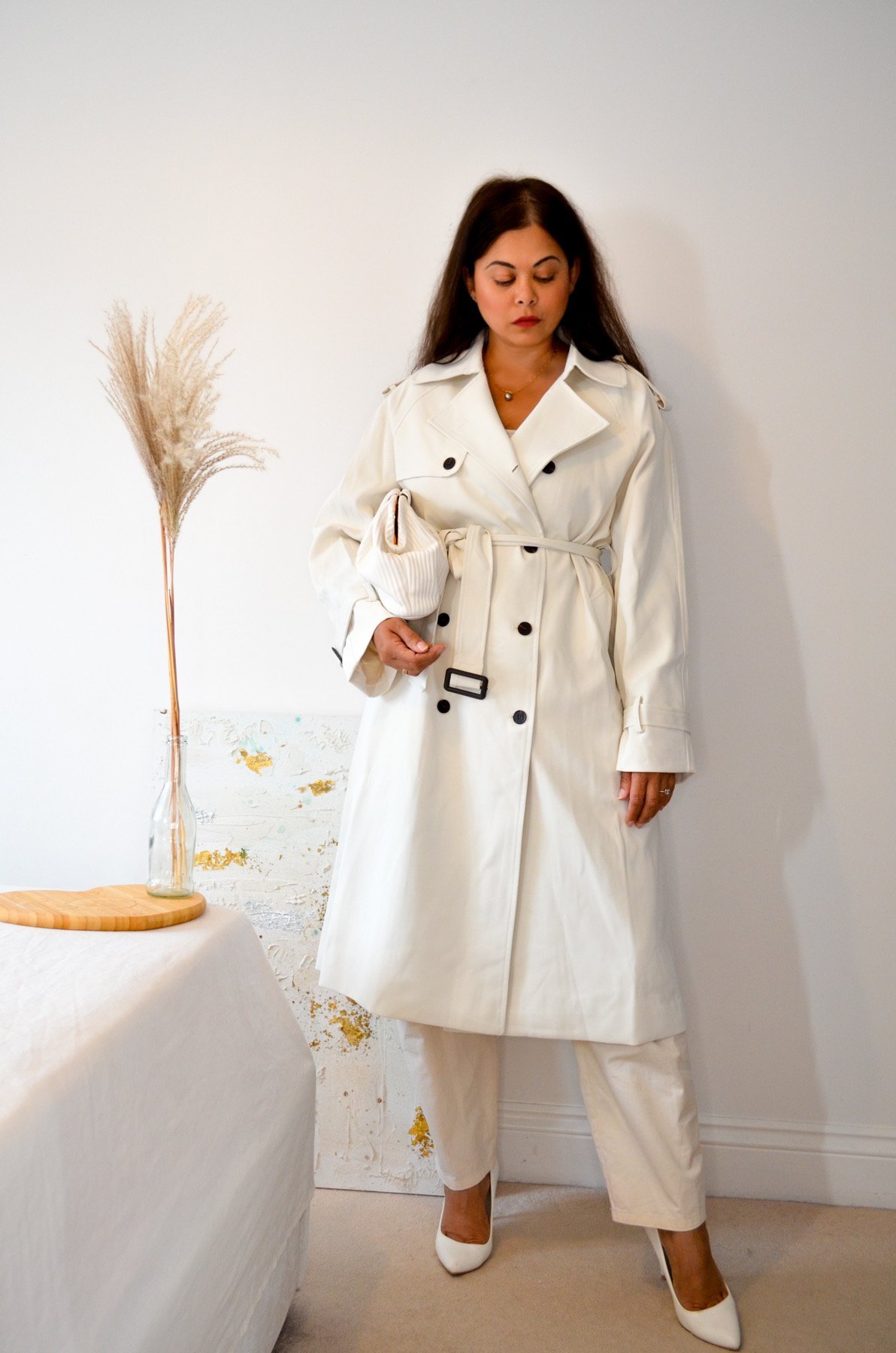 A woman wearing an all white outfit with a white trench coat and white top and trousers for Autumn.