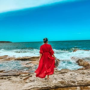 A woman standing on a rocky beach in Sydney Australia, looking into the horizon