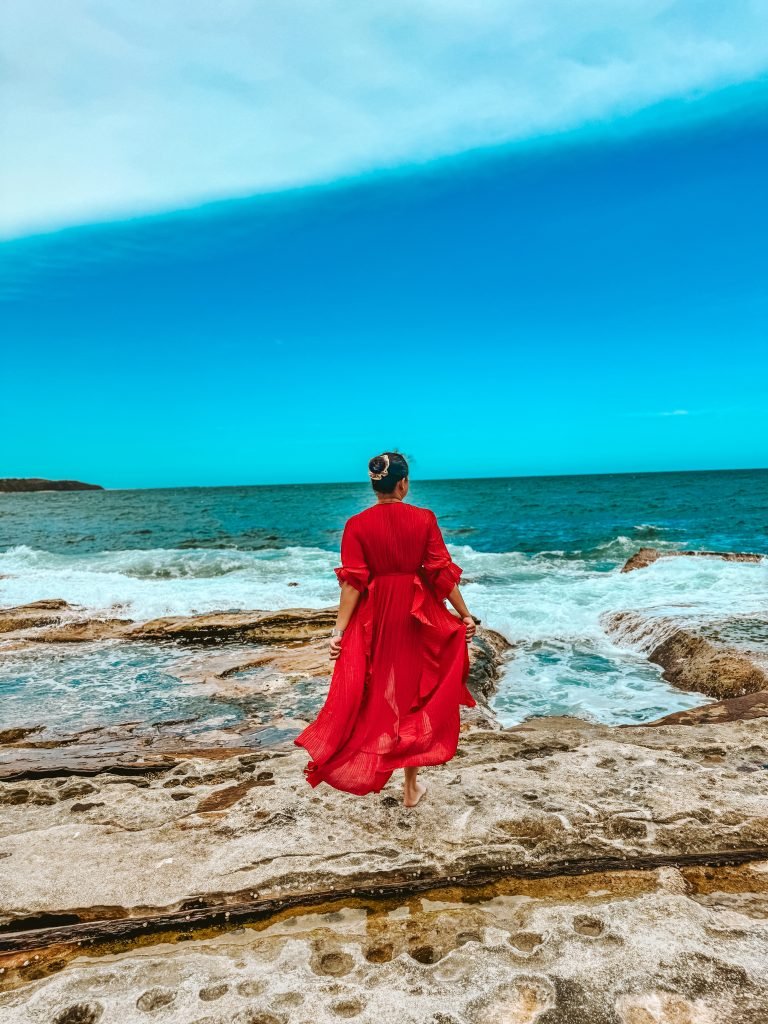 A woman in a red dress looking at the beach 