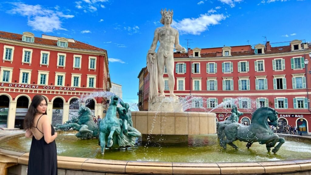 A woman wearing a backless black dress standing in front of a fountain in Nice France.