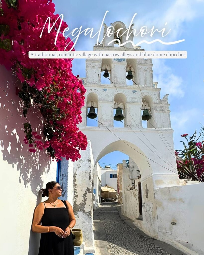 Pooja standing in front of bougainvillea plant in full bloom with the lovely 6 bell archway of a typical Santorini church in the village of Meglahori