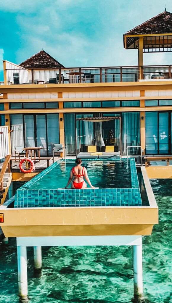 A lady in a red bikini sitting at the edge of an infinity pool of the In ocean villas at Angsana Velavaru Maldives. 