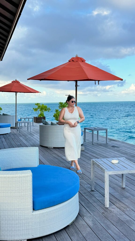 Pooja standing in a Beach dress on the outdoor deck of Azzuro Restaurant at Angsana Velavaru 