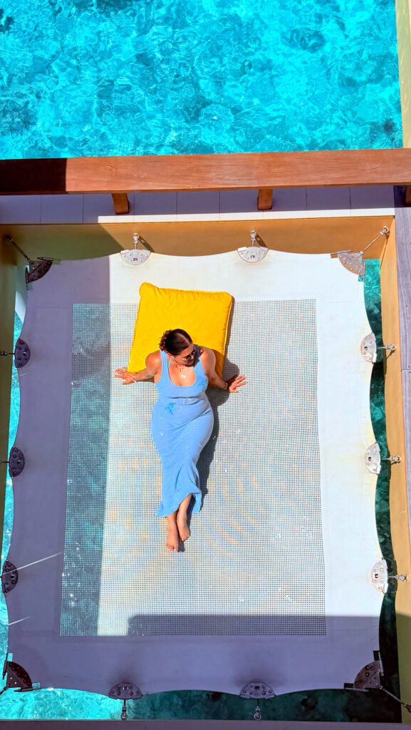 A lady in a blue beach dress laying down on a hammock in a Maldives water bungalow.