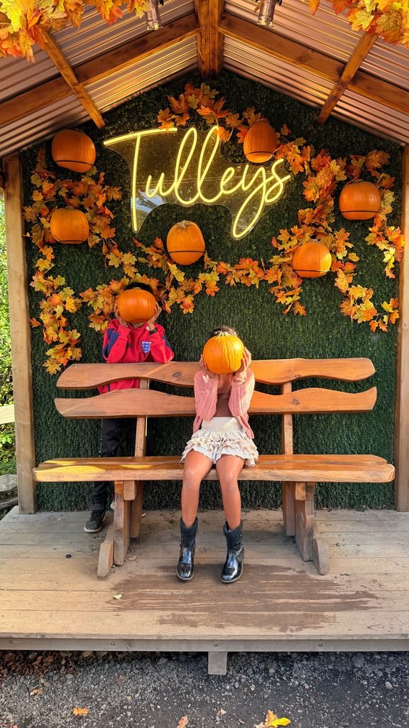 Two children posing playfully with pumpkins covering their faces at Tulleys pumpkin festival.
